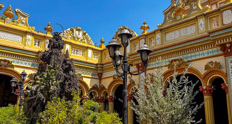 Golden arched courtyard with ornate lamppost and lush greenery inside Vinh Trang Pagoda complex.