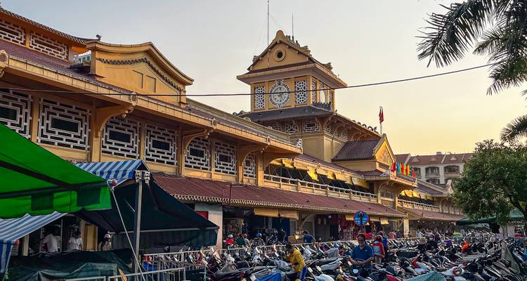 Ben Thanh Market clocktower and crowded rows of parked motorbikes at sunset in Ho Chi Minh City.