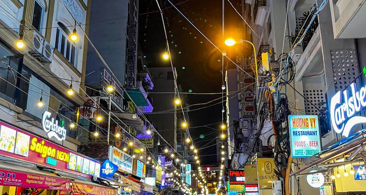 Vibrant night scene of Bui Vien Walking Street with strings of lights, neon signs, and crowds in Ho Chi Minh City.