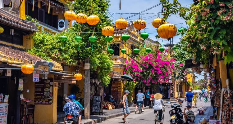 Hoi An’s lantern-lined street with cyclists and blossoming bougainvillea on a sunny day.