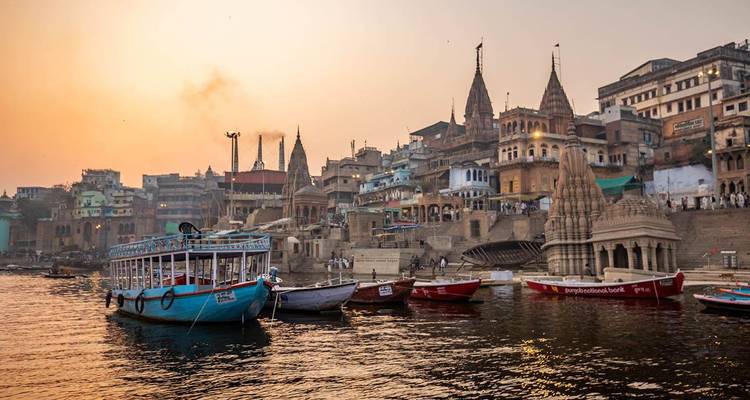 Boote schaukeln neben den antiken Flussufertempeln und Ghats von Varanasi bei warmem Sonnenaufgang
