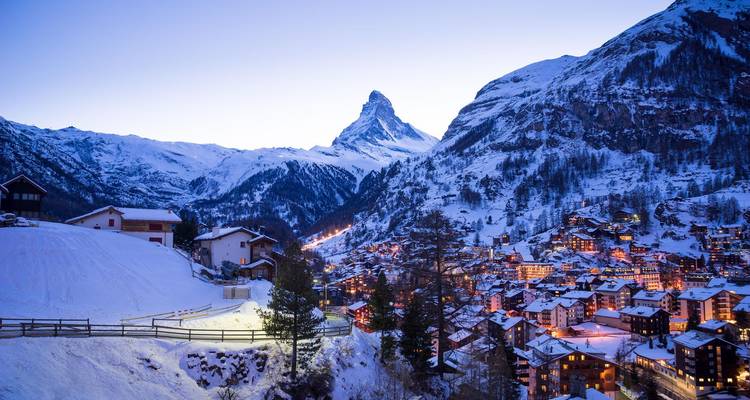 Le village enneigé de Zermatt brille au crépuscule sous l'emblématique Cervin aux pics acérés.