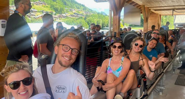 Lächelnde Reisende, die in einer Reihe von Alpenachterbahn-Wagen sitzen und bereit sind, abzufahren.