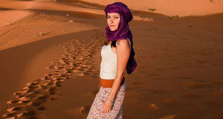 Una mujer con un pañuelo morado se para en las dunas doradas del Sahara durante la luz cálida de la tarde.