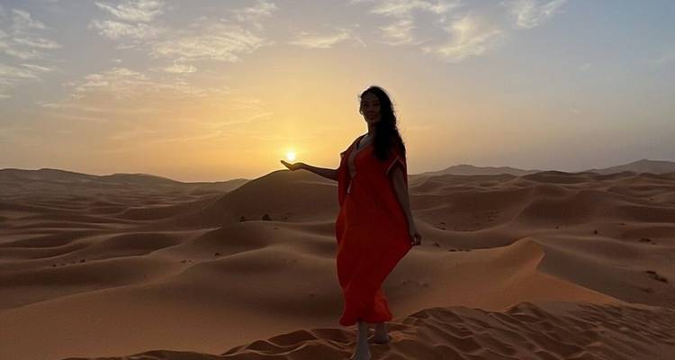 Silhouetted woman in flowing red dress appears to cradle the rising sun over endless dunes.
