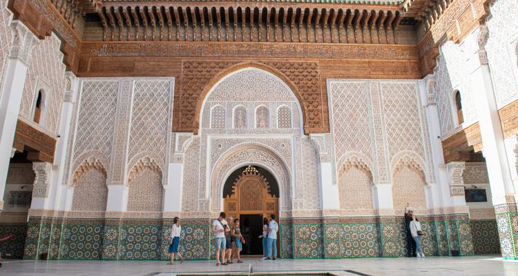 Intricate courtyard of a traditional Moroccan madrasa with visitors admiring tile work.