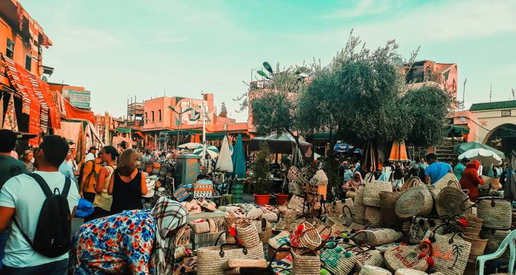 Bustling Marrakesh souk filled with people, colorful stalls and woven baskets under turquoise sky.