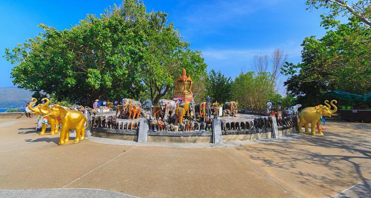 Des statues d'éléphants colorées entourent un sanctuaire situé au sommet d'une colline sous des cieux bleus.