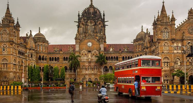 Historic Chhatrapati Shivaji Terminus with a classic red double-decker bus parked in the rain.