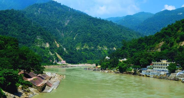 Un large fleuve vert jade serpente à travers les contreforts densément boisés de l'Himalaya sous un ciel bleu éclatant.