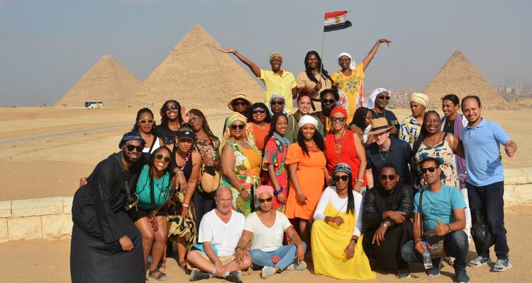 Een grote groep toeristen poseert energiek voor de iconische piramides op een zonnige woestijndag, waarbij iemand een Egyptische vlag hoog in de lucht houdt.