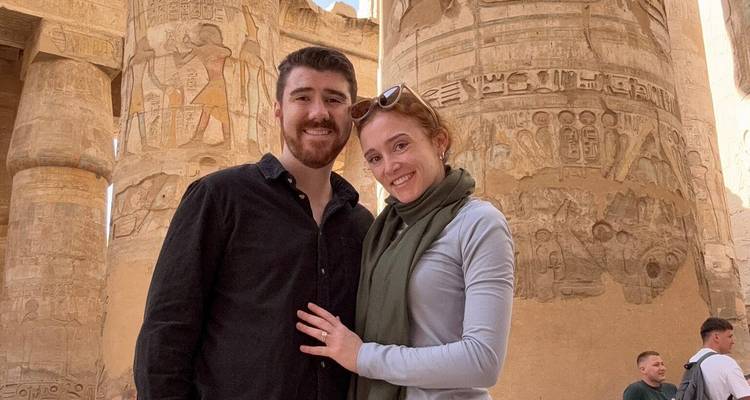Een glimlachend stel staat voor indrukwekkende, met hiëroglieven bedekte zuilen in een oud Egyptische tempel.
