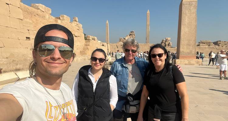 Een groep vrienden maakt een vrolijke selfie tussen obelisken en ruïnes in Karnak Temple onder een heldere blauwe hemel.