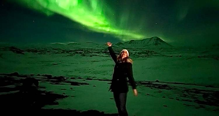 Reisender mit erhobener Hand unter leuchtend grünem Nordlicht über verschneiter Ebene