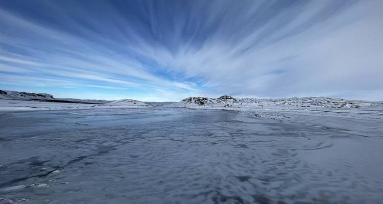 Riesiger gefrorener See unter dramatischen gestreiften Wolkenmustern in einem blassen Himmel