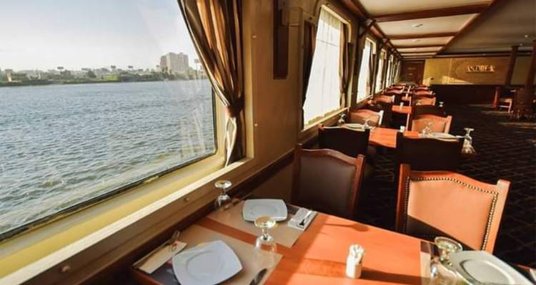 Salon élégant de restauration sur un bateau de croisière du Nil avec de grandes fenêtres donnant sur le fleuve.