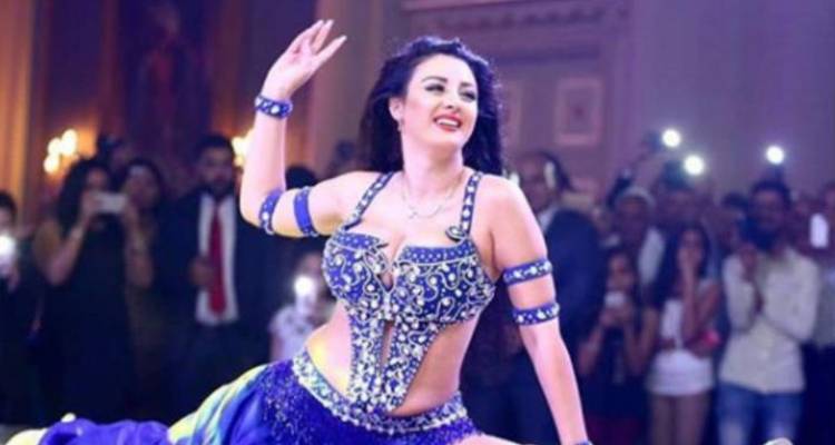 Danseuse du ventre vêtue d'un costume bleu étincelant se produisant sur scène devant un public.