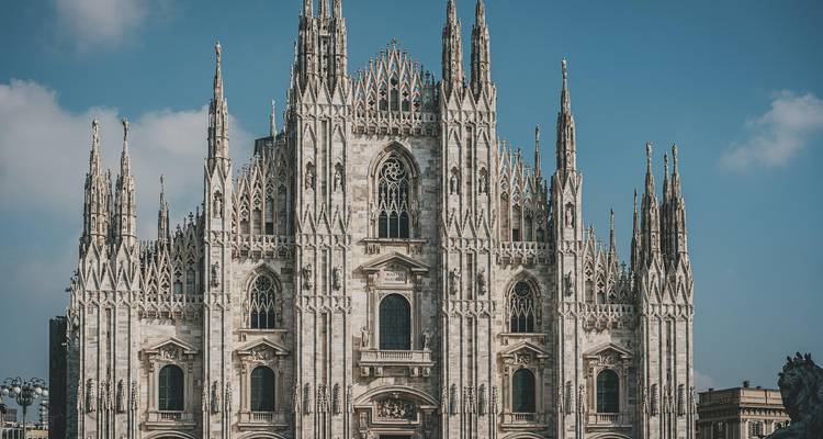 Les flèches de marbre ornées et la façade complexe du Dôme de Milan s'élèvent majestueusement contre un ciel dégagé.