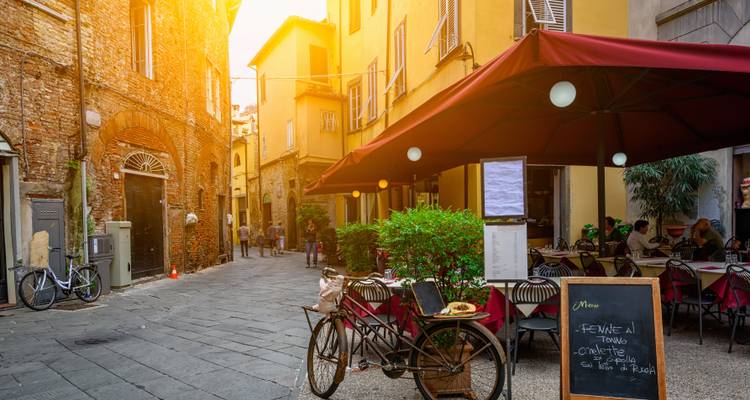 Encantador callejón italiano con mesas de café, una bicicleta vintage y la cálida luz del atardecer.