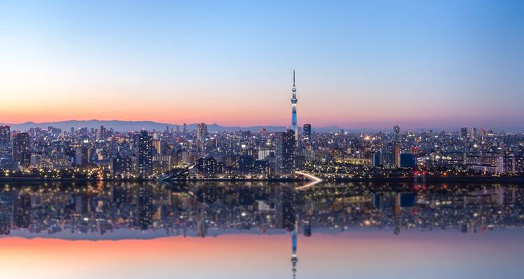 Skyline panoramique de Tokyo au crépuscule avec la Skytree et les lumières de la ville se reflétant sur une rivière calme.