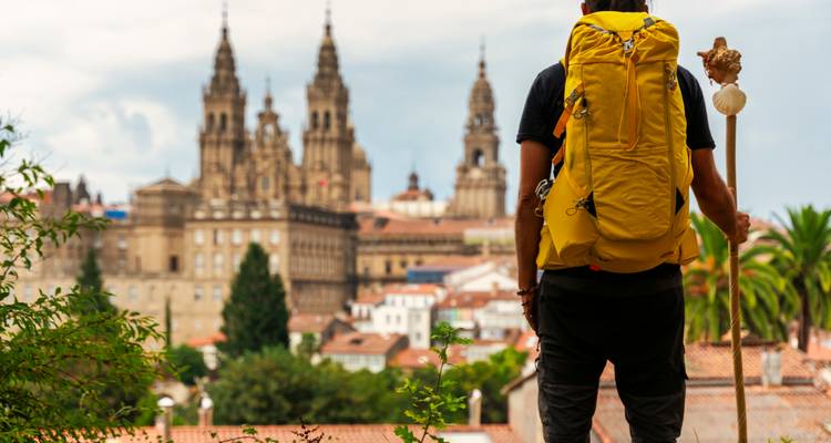 Een pelgrim met een gele rugzak pauzeert voor de verre kathedraalspitsen van Santiago de Compostela.