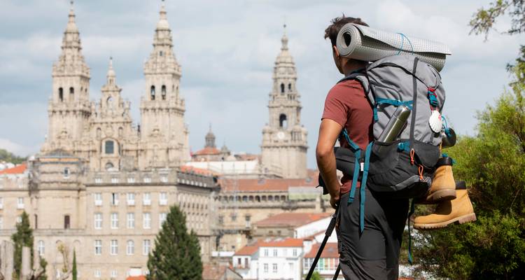 Achteraanzicht van een backpacker met opgerold slaapmat die naar de Santiago-kathedraal kijkt.