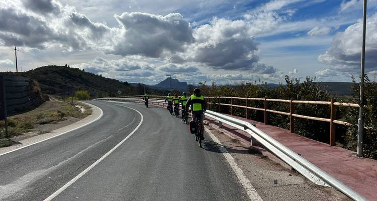Radfahrer in Warnwesten fahren auf einer gewundenen andalusischen Straße unter dramatischem Himmel.