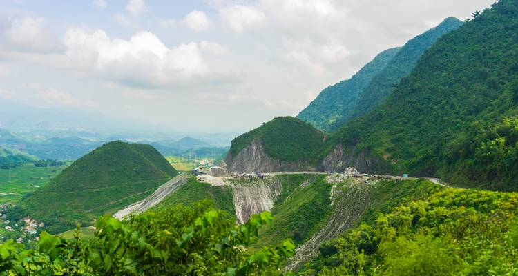 Mountain pass road winding between lush green hills and valleys under cloudy skies