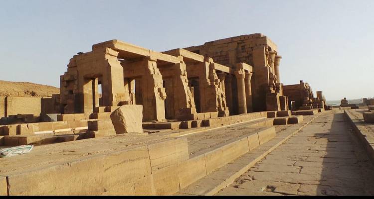 Ruines de temple en grès ancien avec des piliers monumentaux alignés le long d'une longue chaussée en pierre à la lumière de l'après-midi éclatante.