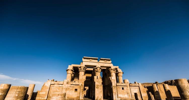 Grande façade d'un ancien temple égyptien encadrée contre un ciel bleu profond avec un vaste avant-plan dégagé.