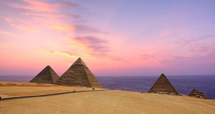 De piramides van Giza tekenen zich af tegen een levendige roze en paarse zonsondergangshemel.