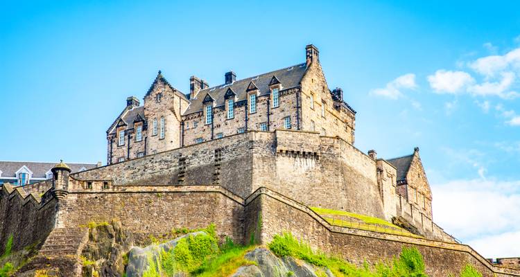 Das imposante Steinschloss Edinburgh Castle thront auf seinem felsigen Vorsprung vor einem leuchtend blauen Himmel.