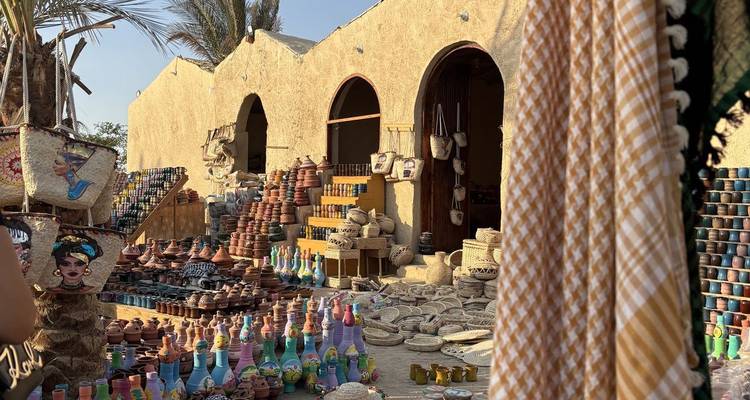 Un marché désertique en plein air expose de la poterie colorée, des bouteilles et des objets artisanaux tissés contre des arches en adobe.