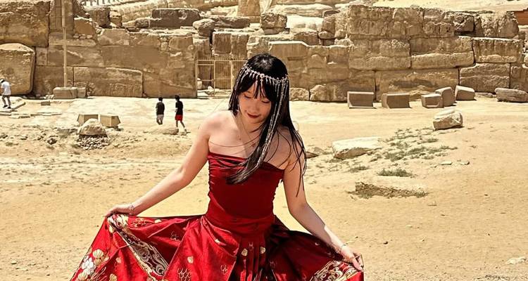 Woman in a red dress twirling in front of ancient stone blocks and desert landscape near the pyramids.