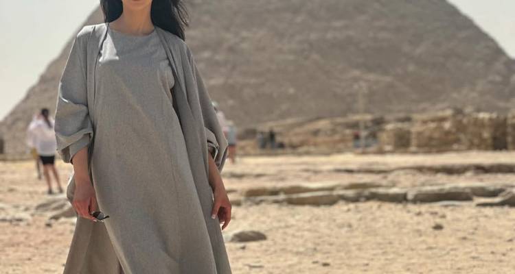 Stylish woman in grey dress posing before a pyramid on a hazy desert afternoon.