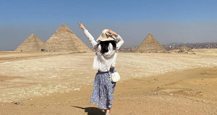 Traveler walking toward the three pyramids with arms raised in a vast desert expanse.