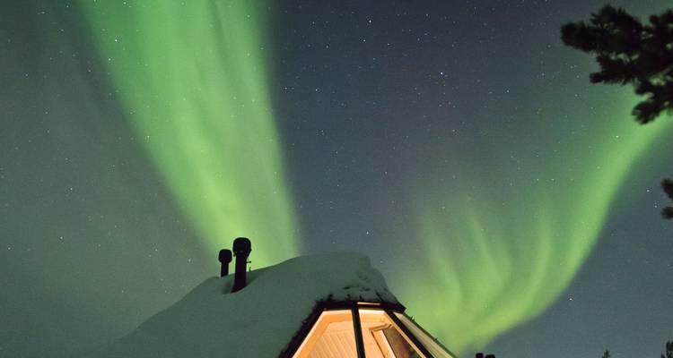 Brilliant green aurora borealis dancing above a snow-topped glass igloo roof under starry night sky.
