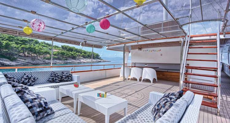Open sundeck lounge on yacht with white wicker seating, colorful lanterns, and sea views.