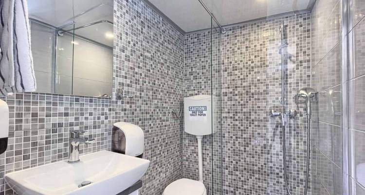 Compact modern bathroom with mosaic tile walls, white sink, mirror cabinet, toilet and glass shower enclosure.