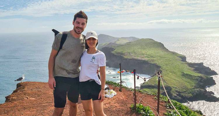 Couple souriant se tenant au bord d'une falaise dominant des promontoires verdoyants spectaculaires et l'océan Atlantique