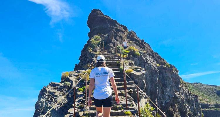 Vue arrière d'une femme montant des marches en pierre escarpées sur une crête de montagne rocheuse contre un ciel bleu éclatant