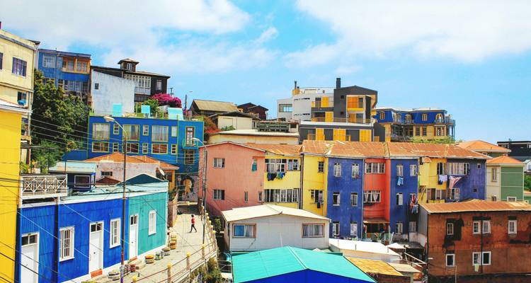 Brightly painted houses cascade down a steep street in Valparaiso under patches of blue sky.
