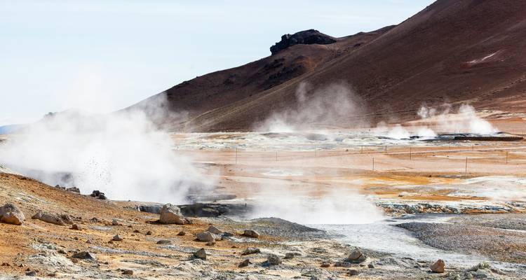 Multiple fumaroles vent steam across a barren high-altitude desert surrounded by brown mountains.