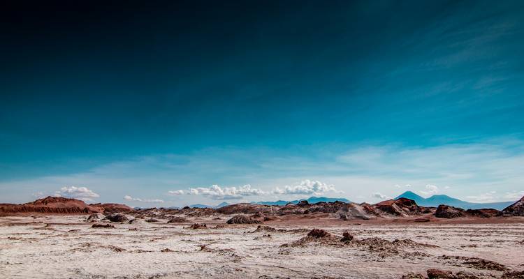 Expansive Atacama desert plain beneath a vast deep-blue sky with distant volcanic ridges.