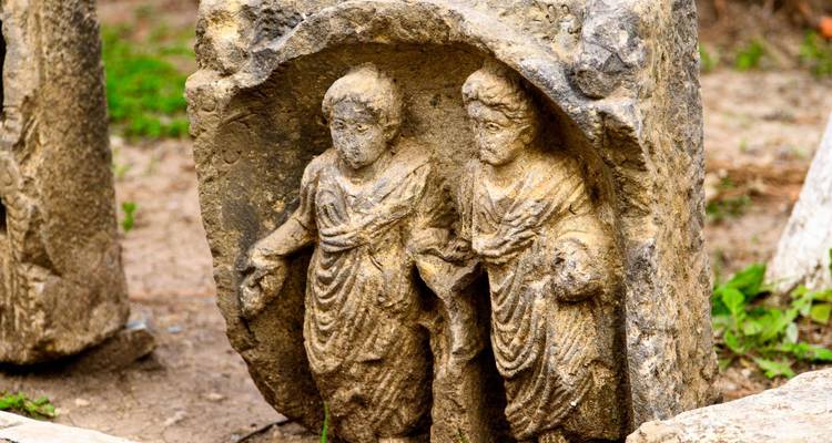 Verweerde stenen relief met daarop twee in gewaden gehulde Romeinse figuren.