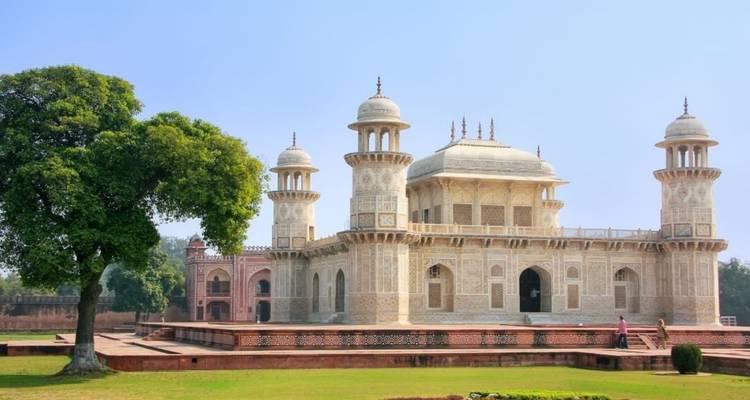 Elegant sandstone and marble Itimad-ud-Daulah Mausoleum (Baby Taj) set within manicured lawns under clear sky.