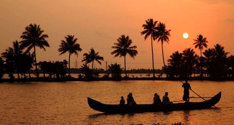 Silhouetted canoe with rower and passengers gliding across calm backwaters at orange sunset framed by palm trees.