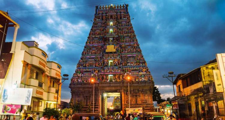 Towering, vividly painted gopuram of a South Indian temple lit at dusk with bustling street activity below.