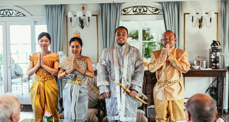 Performers in kleurrijke Khmer ceremoniële kleding staan in een gracieuze groethouding in een helder ingerichte hut.