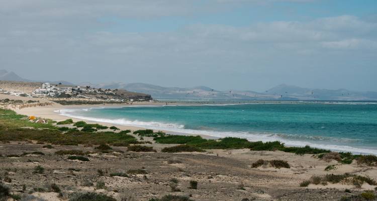 Lange Sandküste mit türkisfarbenem Meer und entfernten Kitesurfern